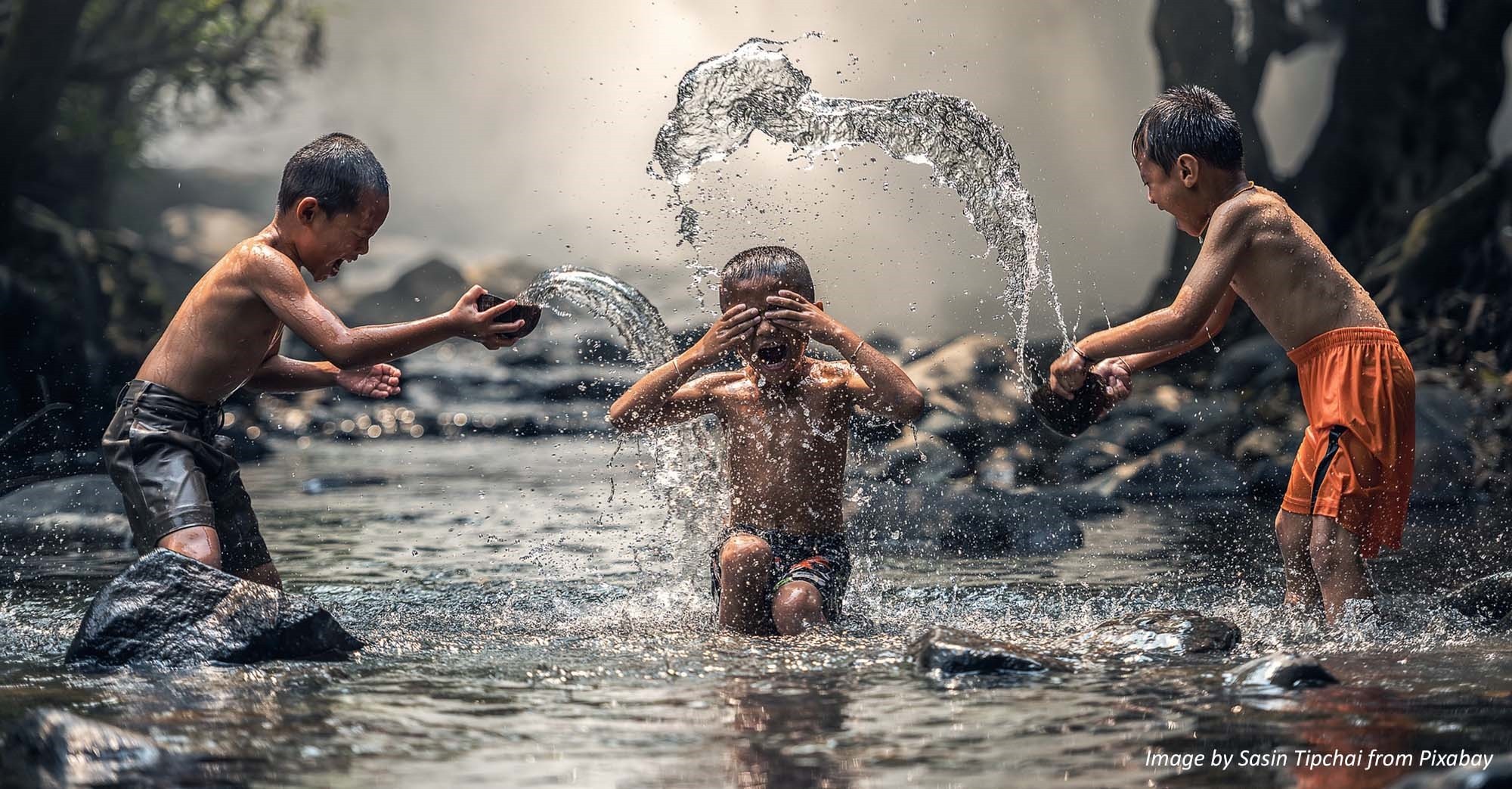 Three young boys joyfully throw water over each other whilst playing in a river